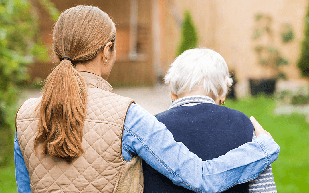 Photo of the back of two women. The younger one has her arm around the elderly woman. Photo de dos de deux femmes. La plus jeune a son bras autour de la femme âgée.