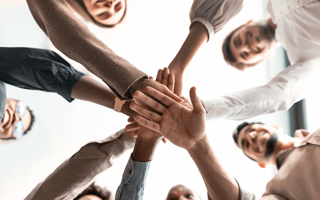 Below view of diverse group of smiling people putting their hands together, standing in circle. Ci-dessous, vue d'un groupe diversifié de personnes souriantes mettant leurs mains ensemble, debout en cercle.